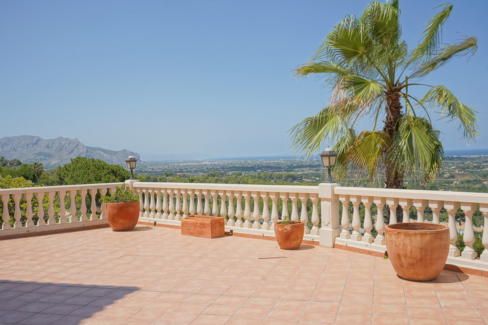 Terrasse surélevée avec sol en terre cuite et balustrade blanche, offrant une vue panoramique sur la vallée et la mer Méditerranée au loin.
