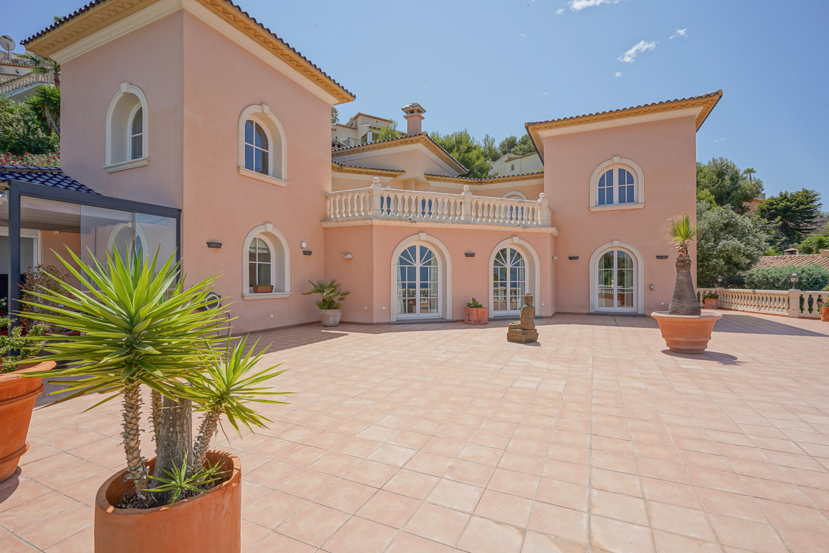 Vaste terrasse extérieure avec carrelage en terre cuite, fenêtres à arcades blanches et façade saumonée aux détails classiques.