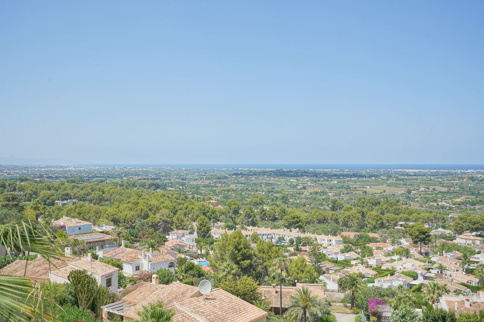 Vue panoramique depuis la terrasse sur la vallée et la mer Méditerranée, soulignant la végétation luxuriante et les toits en terre cuite de La Sella.