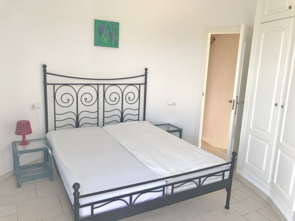 Chambre double avec cadre de lit en fer forgé noir, placards intégrés blancs et sol en carrelage clair. Une porte ouverte mène à la salle de bain.