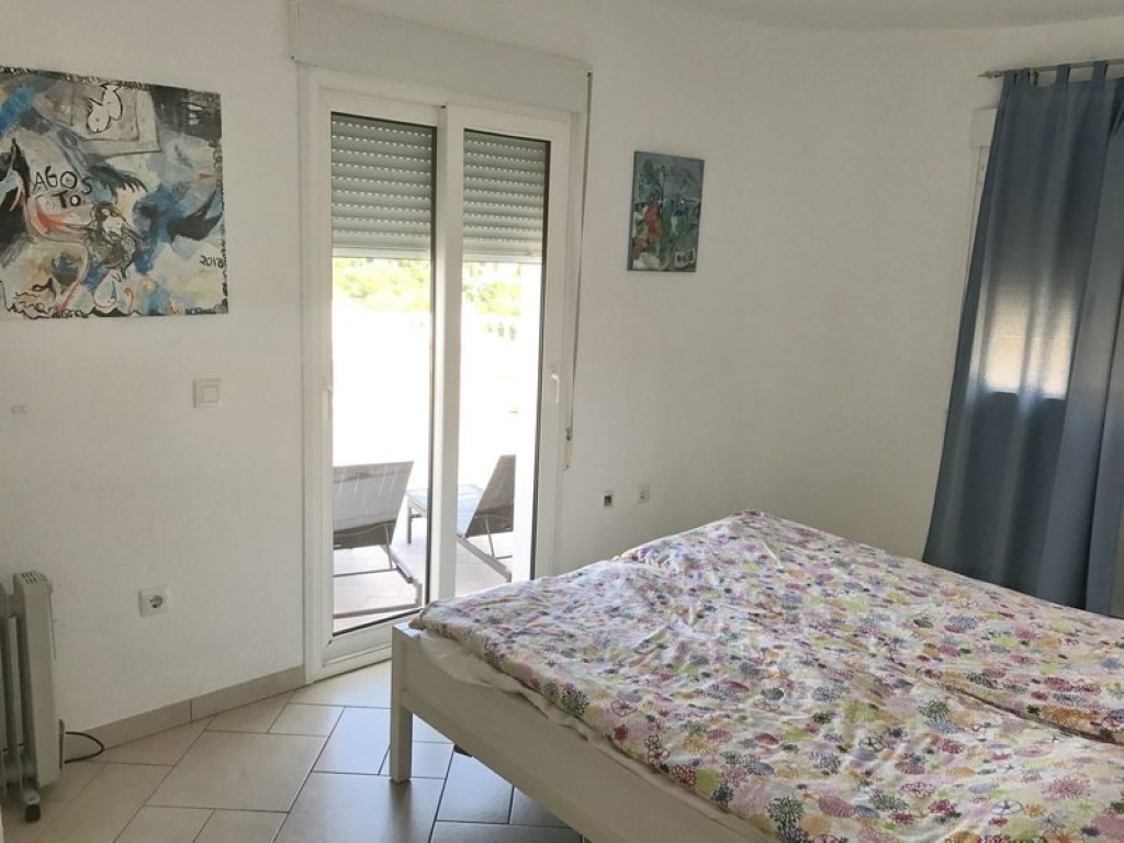 Chambre lumineuse avec carrelage au sol, décorée d'œuvres d'art et offrant un accès direct à la terrasse par une grande porte vitrée coulissante.