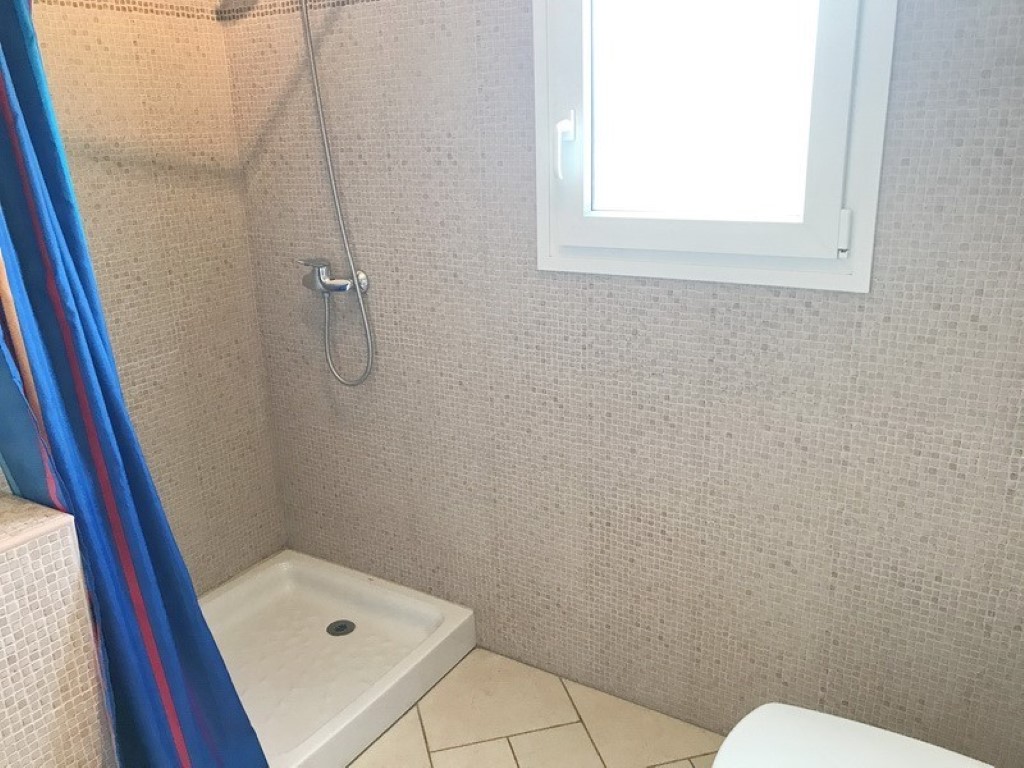 Espace douche avec murs en mosaïque beige, receveur blanc et fenêtre givrée offrant une luminosité naturelle tout en préservant l'intimité.