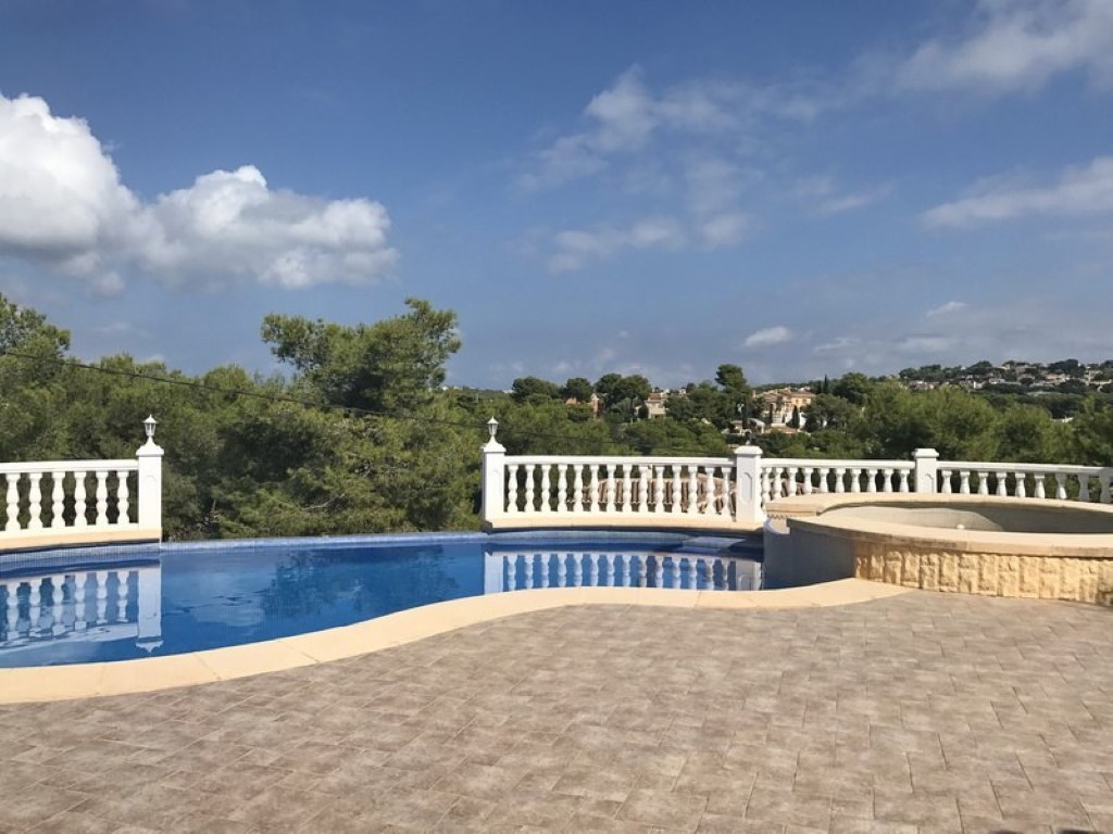Piscine aux formes arrondies avec jacuzzi attenant, terrasse pavée et balustrade blanche offrant une vue panoramique sur la pinède environnante.