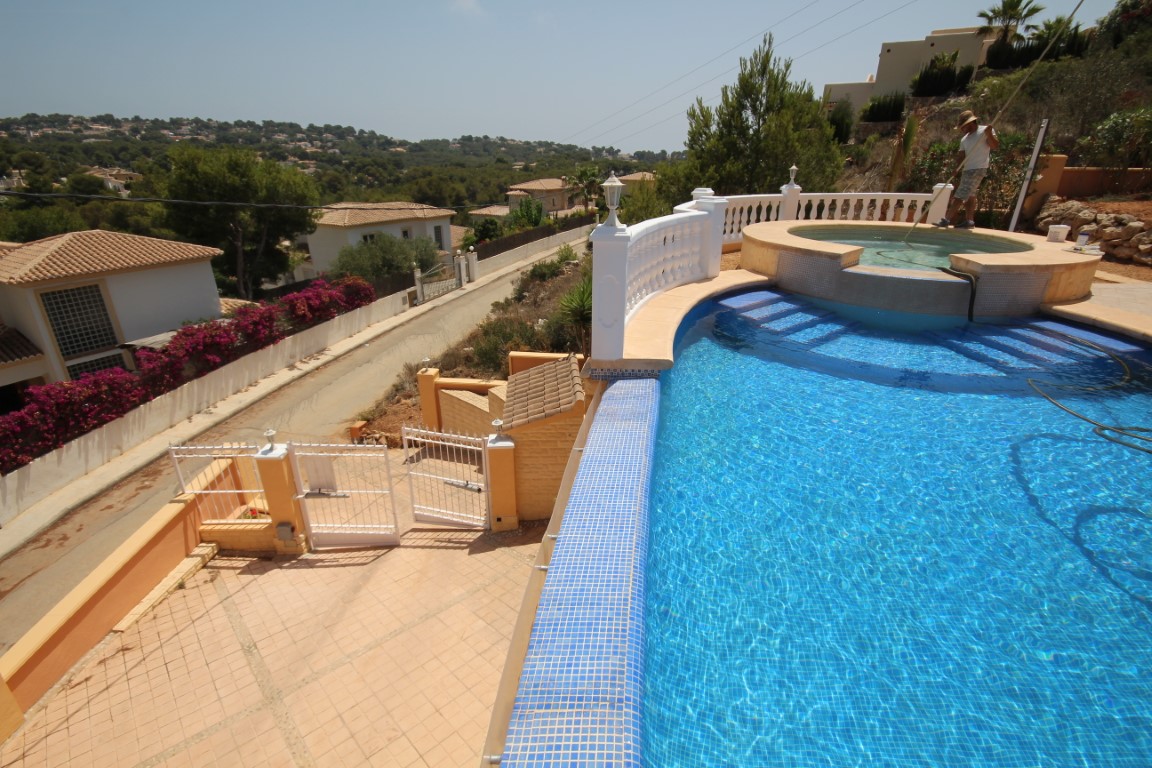 Piscine surélevée avec mosaïque bleue et jacuzzi circulaire intégré, entourée d'une balustrade blanche offrant une vue panoramique sur la vallée de Javea.