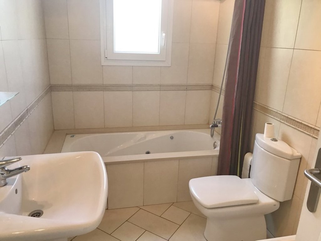 Salle de bain équipée d'une baignoire balnéo encastrée, d'un lavabo en céramique blanche et de carrelage mural beige avec une bordure décorative élégante.