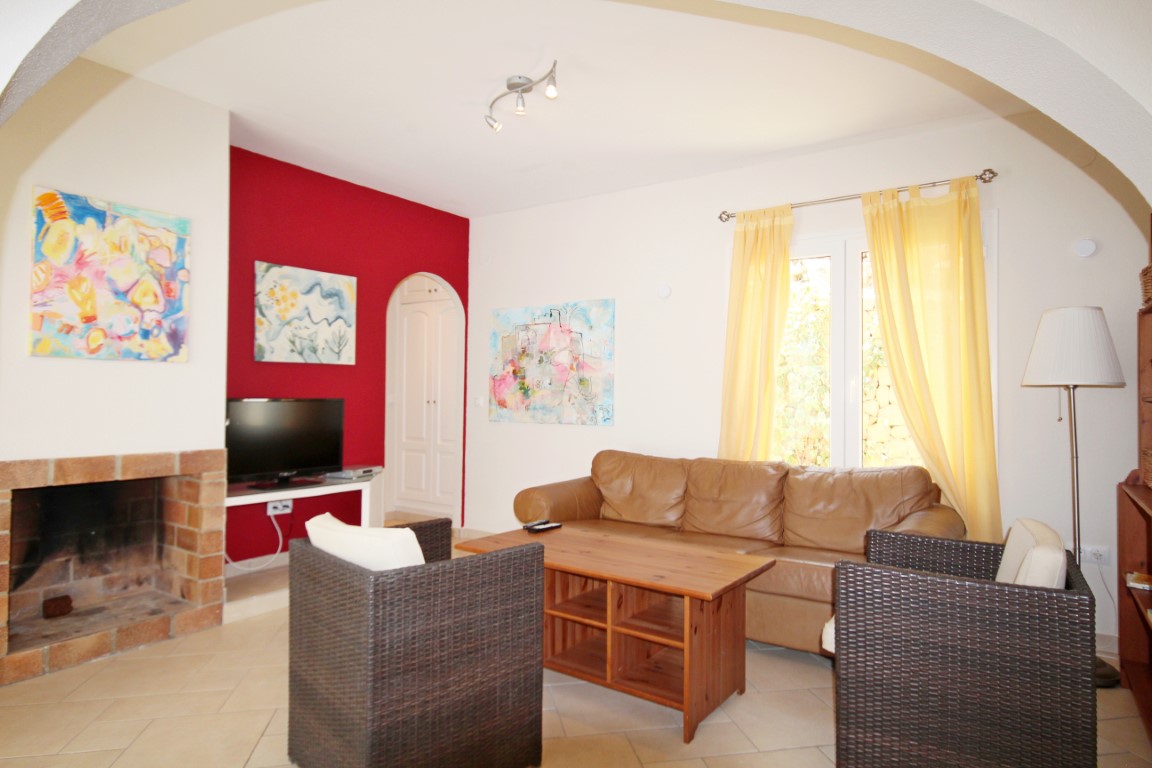 Salon avec cheminée en brique, mur d'accent rouge et canapé en cuir. Comprend des fauteuils en osier, une table basse en bois et une lumière naturelle avec rideaux jaunes.