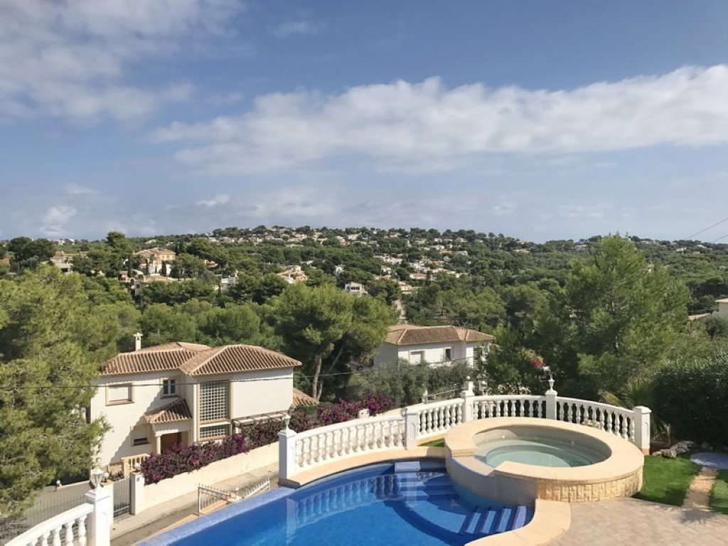 Terrasse surélevée avec piscine en mosaïque bleue et jacuzzi circulaire intégré, offrant une vue panoramique sur les collines boisées et les villas de Javea.