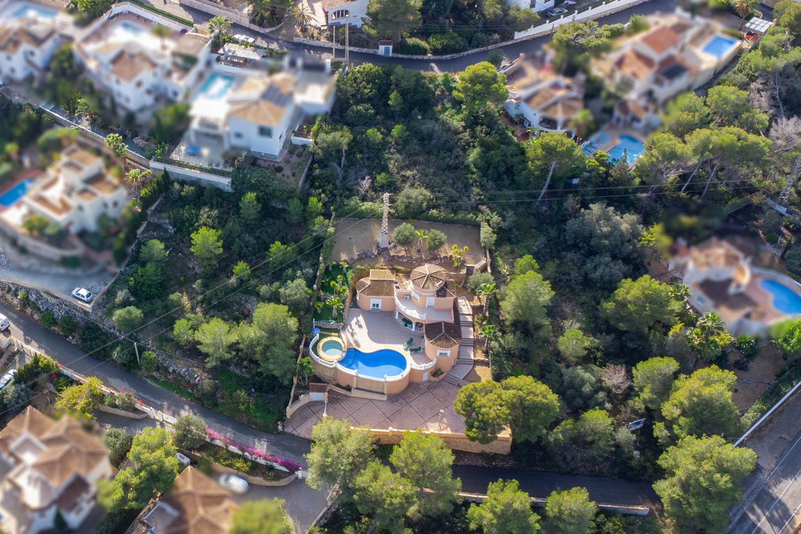 Vue aérienne de la villa méditerranéenne présentant la piscine de forme libre, le jacuzzi circulaire et les vastes terrasses pavées au cœur d'une pinède.