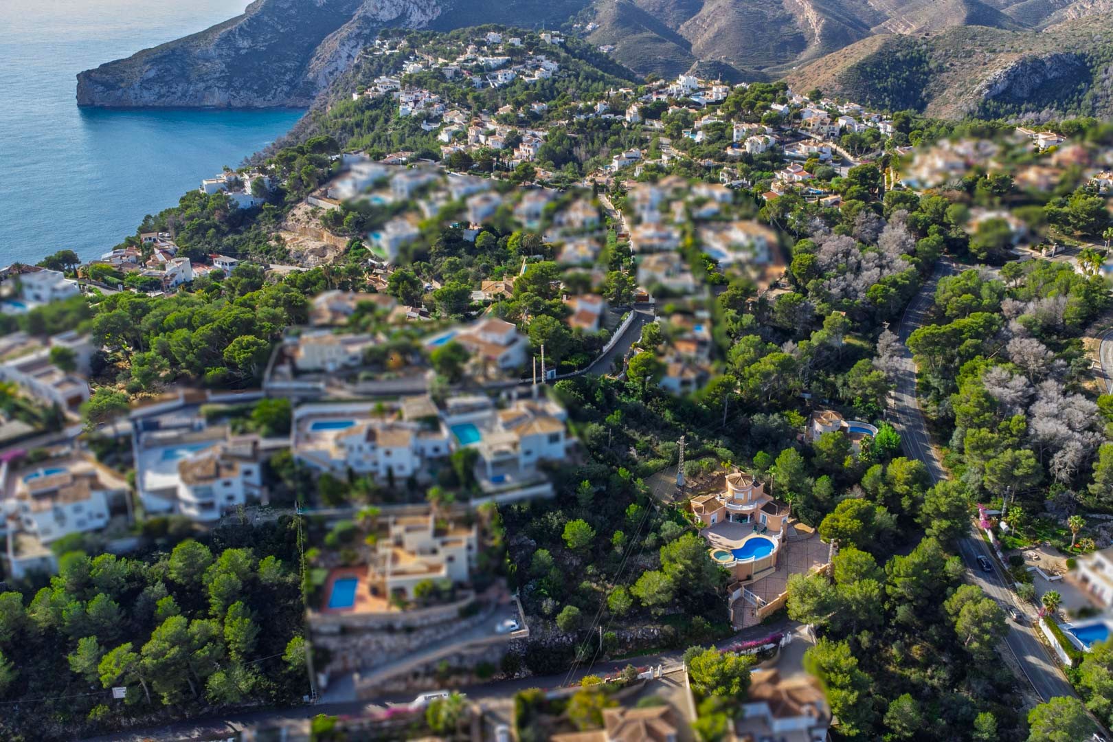 Vue aérienne d'un quartier résidentiel à Javea, présentant des villas méditerranéennes avec piscines nichées dans une pinède dense bordant le littoral.