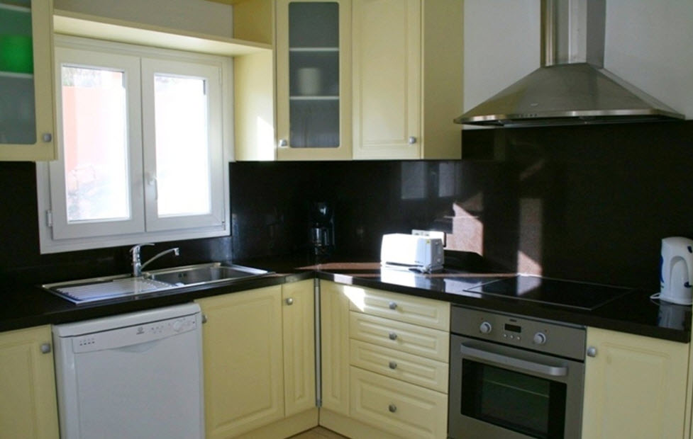 Cuisine équipée avec des meubles de couleur crème, un plan de travail en granit sombre et des appareils intégrés. Elle dispose d'une plaque vitrocéramique et d'un four en inox.