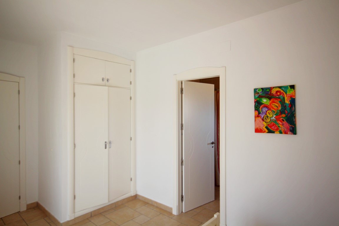 Espace chambre avec placard intégré blanc, carrelage rustique au sol et porte ouverte menant à une pièce attenante.