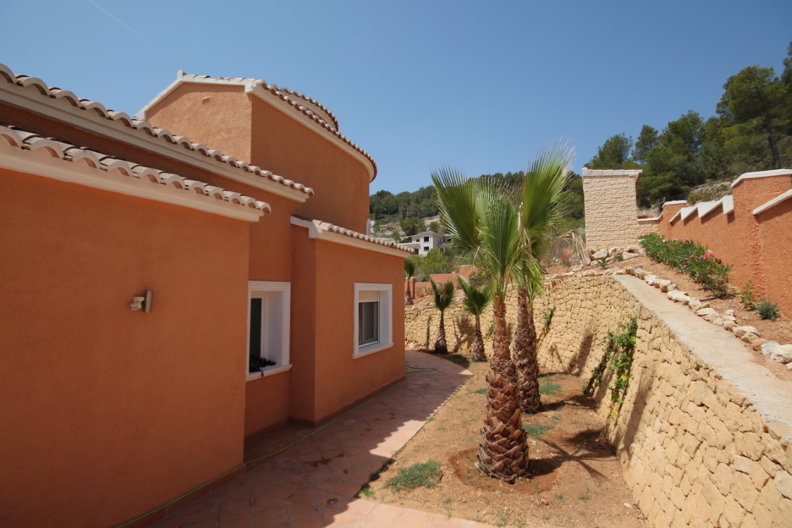Façade aux tons terre cuite avec toiture en tuiles traditionnelles, agrémentée d'un jardin de palmiers et de murs de soutènement en pierre naturelle.