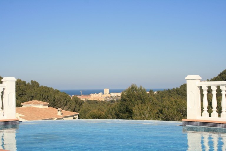 Piscine à débordement avec mosaïque bleue offrant une vue panoramique sur la mer Méditerranée et le paysage côtier de Javea bordé de pins.
