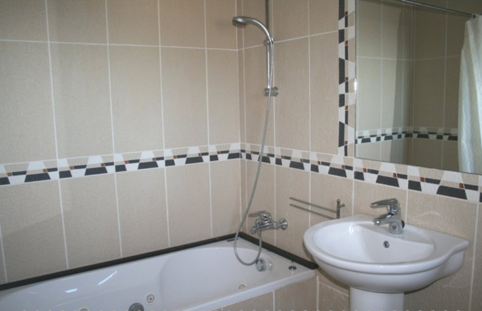 Salle de bains avec baignoire d'hydromassage, lavabo sur pied et carrelage mural beige agrémenté d'une frise géométrique.