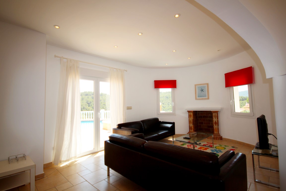 Salon avec canapés en cuir sombre, cheminée décorative et accès direct à la terrasse. La pièce dispose d'un mur courbe et d'un éclairage intégré au plafond.