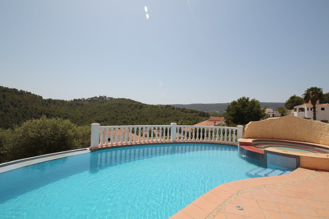 Terrasse ensoleillée avec piscine à débordement et jacuzzi intégré, bordée d'une balustrade blanche offrant une vue dégagée sur les collines.