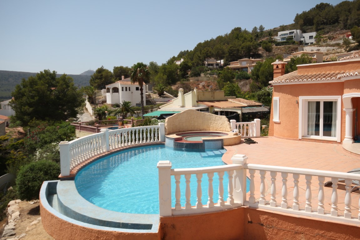 Terrasse solarium comprenant une piscine à débordement en mosaïque bleue, un jacuzzi intégré avec mur en pierre et une balustrade blanche.