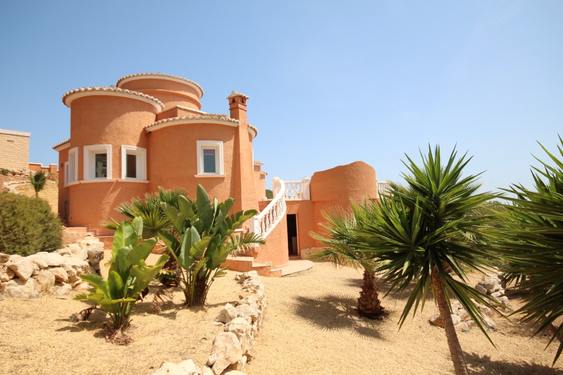 Villa aux formes circulaires de couleur terre cuite avec escalier extérieur à balustrade blanche et jardin méditerranéen composé de gravier et de yuccas.