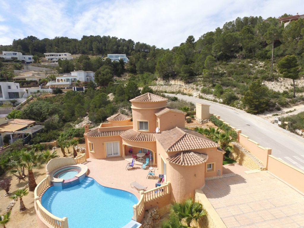 Vue aérienne de la villa méditerranéenne avec sa façade terre cuite, sa piscine aux formes arrondies avec jacuzzi intégré et sa grande terrasse ensoleillée bordée de pins.