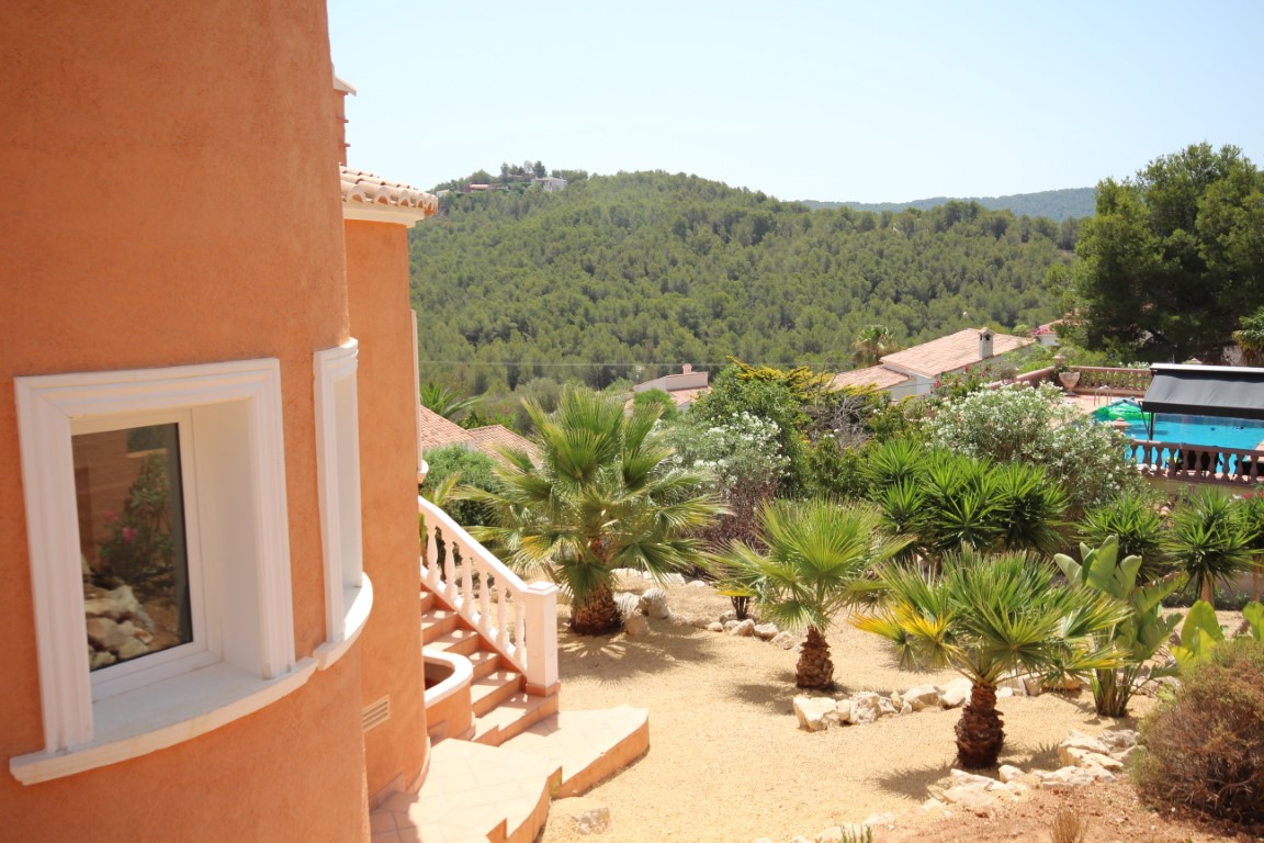 Vue extérieure de la façade incurvée aux tons terre cuite avec jardin méditerranéen, palmiers et vue dégagée sur la vallée boisée environnante.