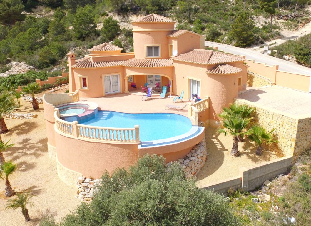 Vue extérieure de la villa méditerranéenne avec piscine à débordement incurvée, jacuzzi intégré et terrasse ensoleillée bordée de palmiers.