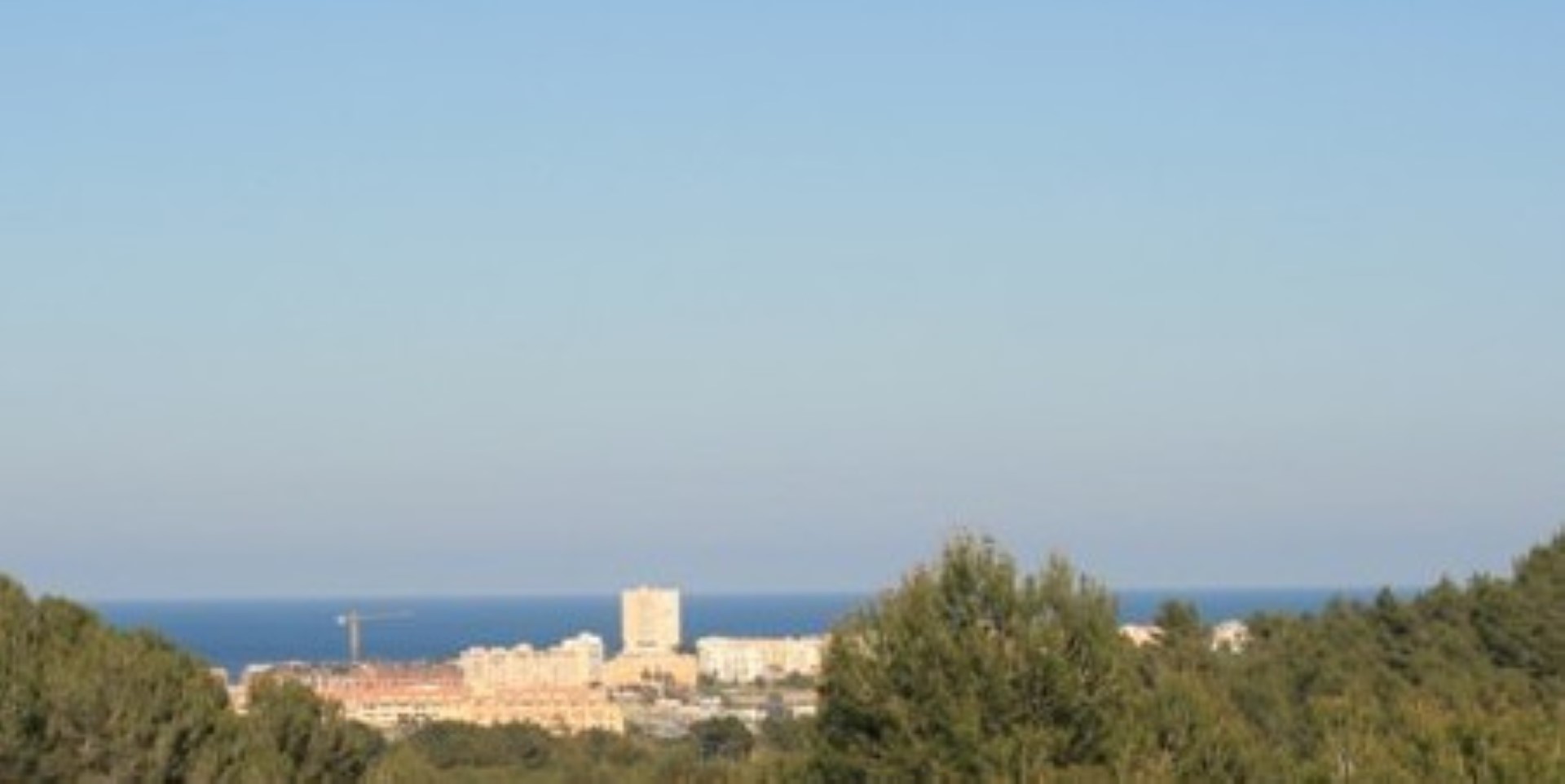 Vues panoramiques sur la mer Méditerranée et la ville côtière depuis la propriété, encadrées par une pinède locale sous un ciel dégagé.
