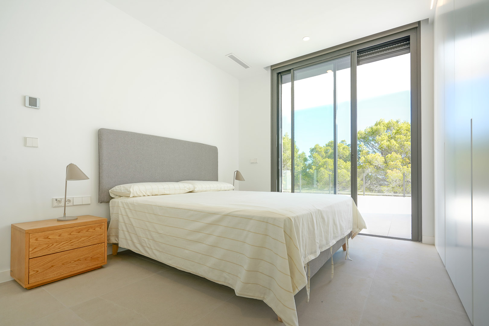 Chambre lumineuse avec placards intégrés, grandes baies vitrées coulissantes et accès direct à la terrasse offrant une vue sur la zone boisée.