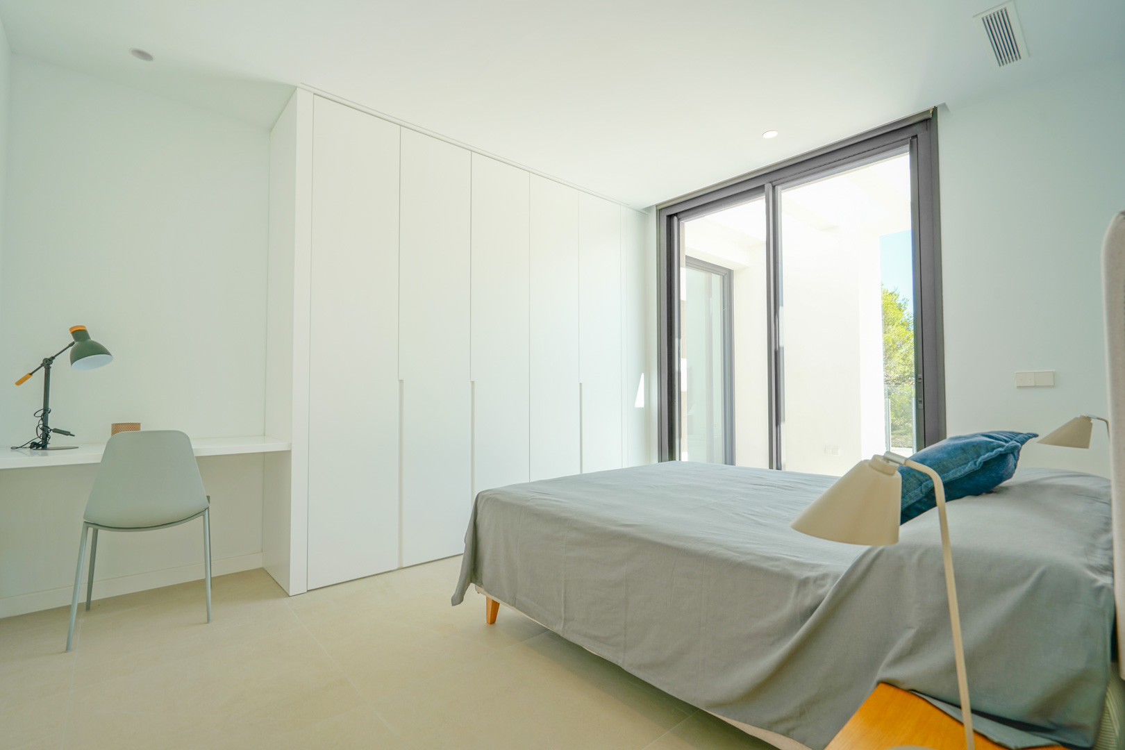 Chambre minimaliste avec placards intégrés blancs, bureau intégré et accès direct à la terrasse par de grandes baies vitrées coulissantes.