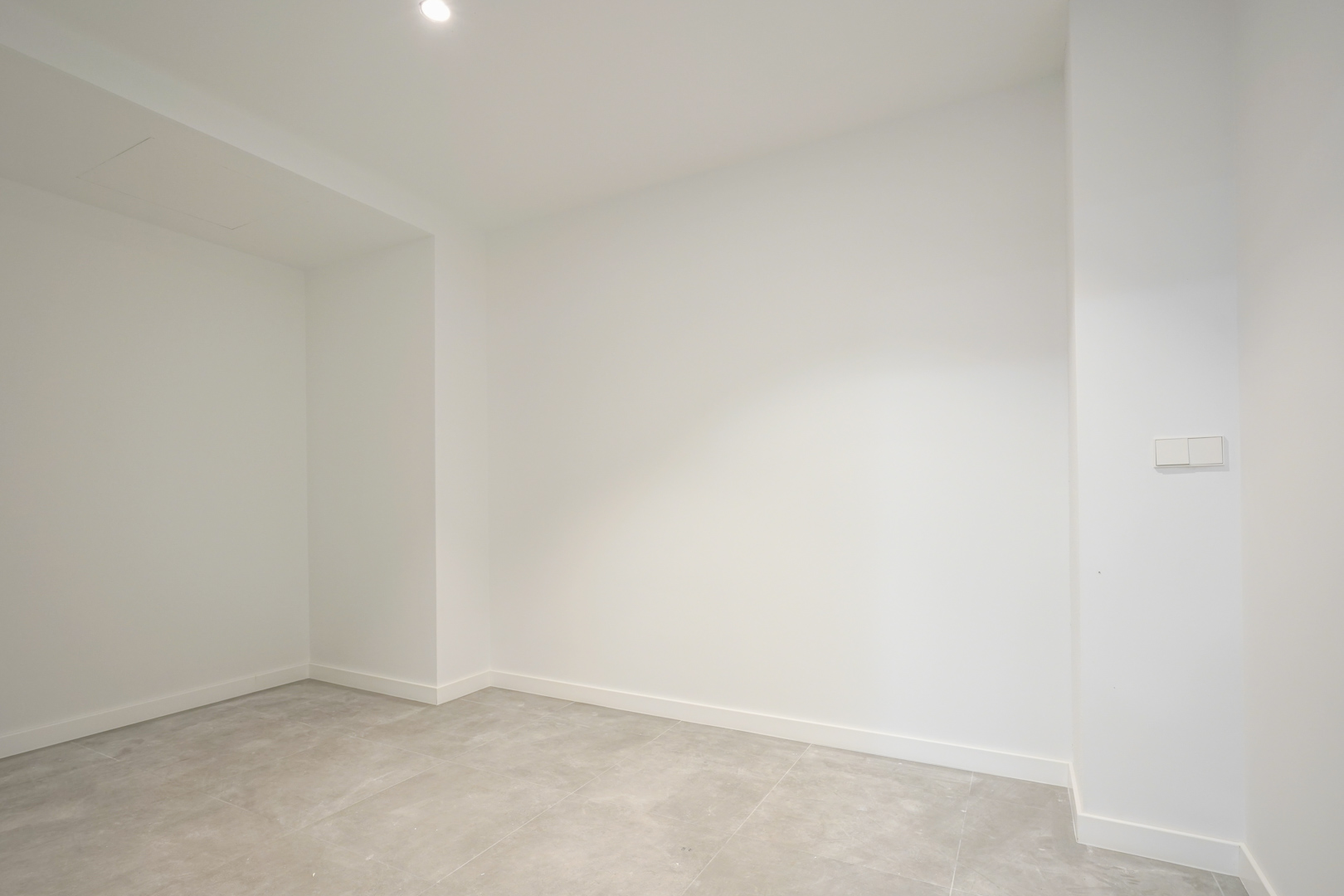 Espace intérieur polyvalent avec murs blancs, sol en grès cérame gris et éclairage encastré, idéal pour un rangement ou un local technique au rez-de-chaussée.