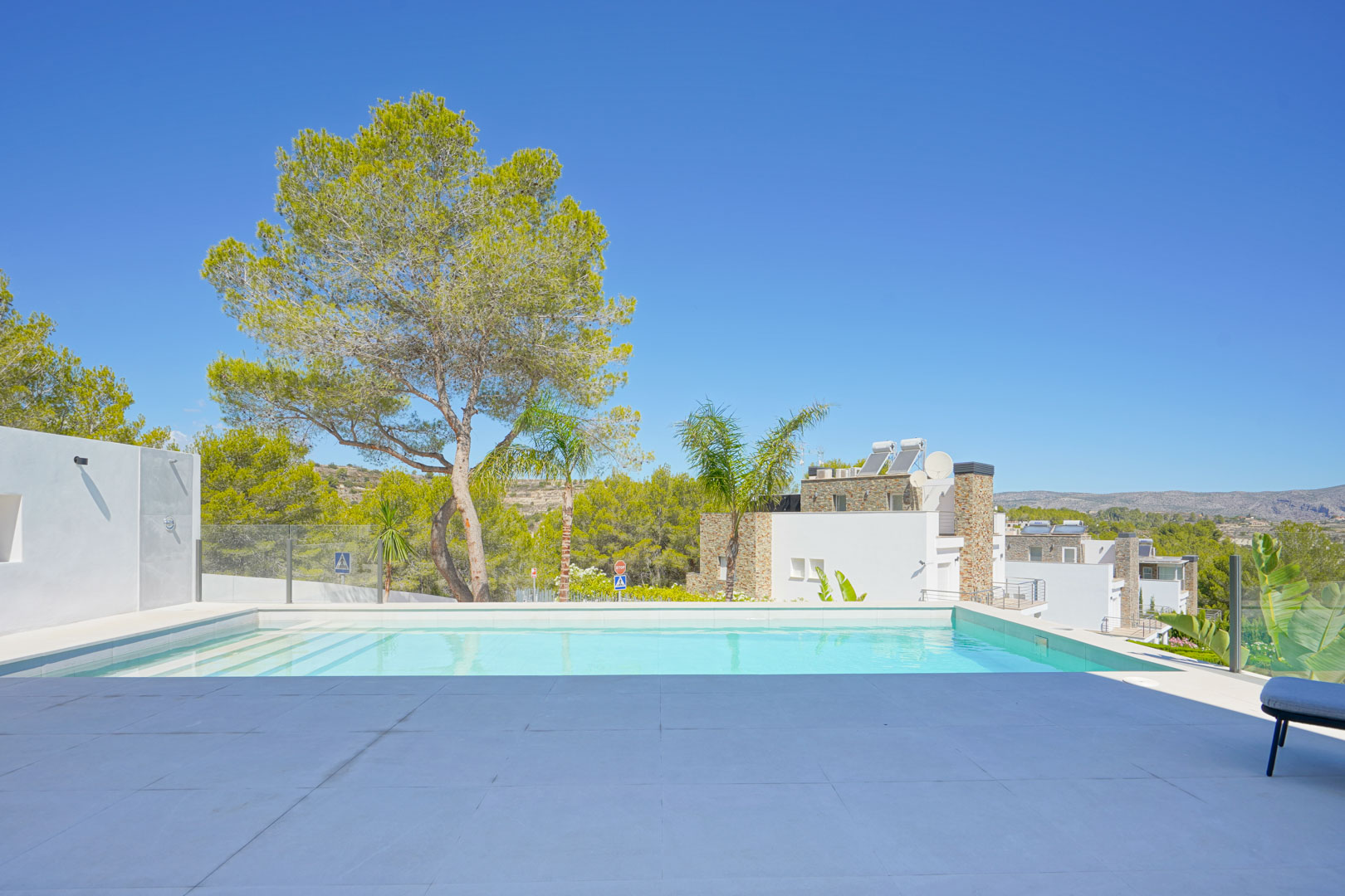 Piscine à débordement avec revêtement blanc et terrasse en dalles grand format, offrant une vue dégagée sur les pins et le paysage environnant.