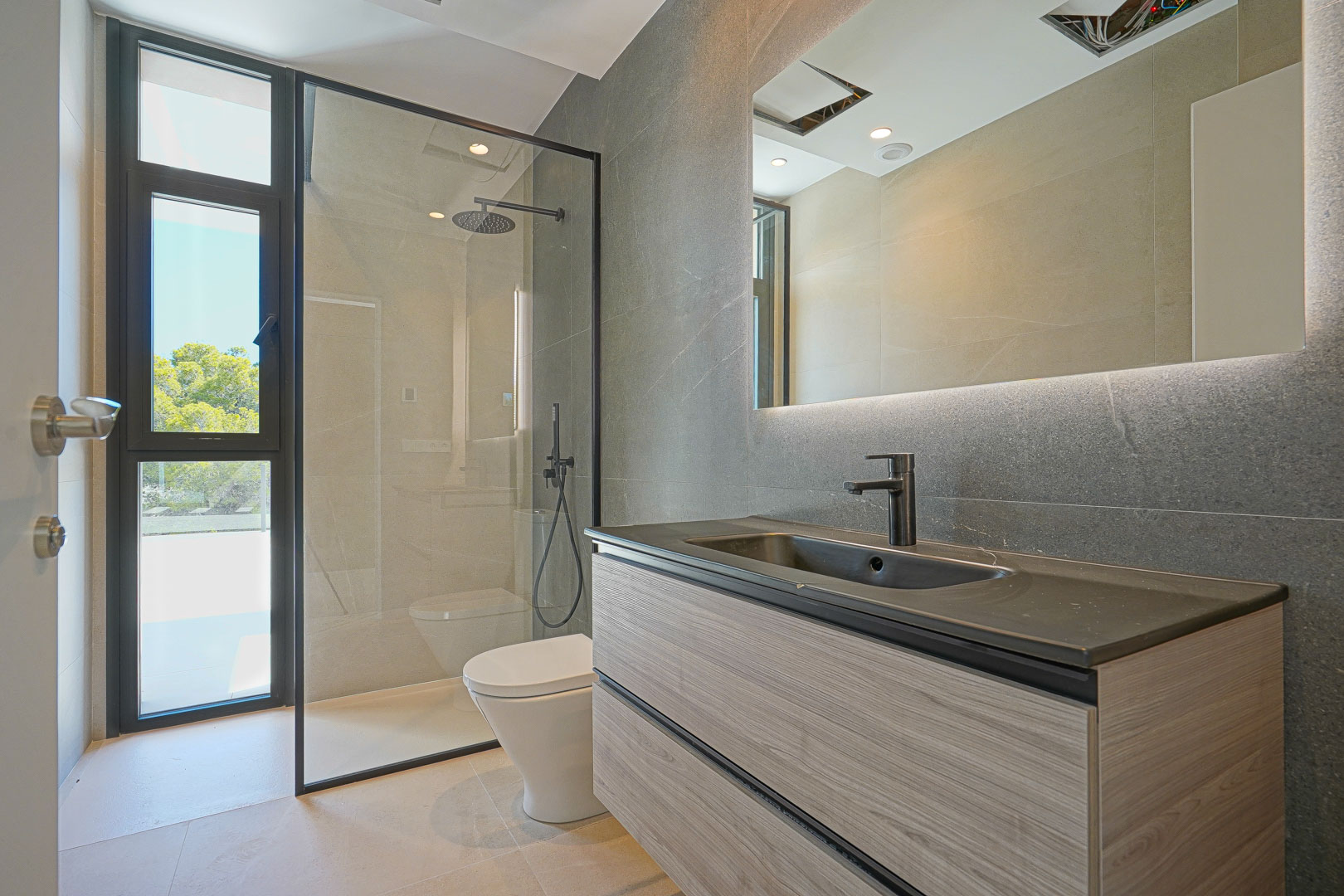 Salle de bain moderne avec meuble vasque suspendu en bois, miroir rétroéclairé et douche à l'italienne avec paroi vitrée à cadre noir et vue dégagée.