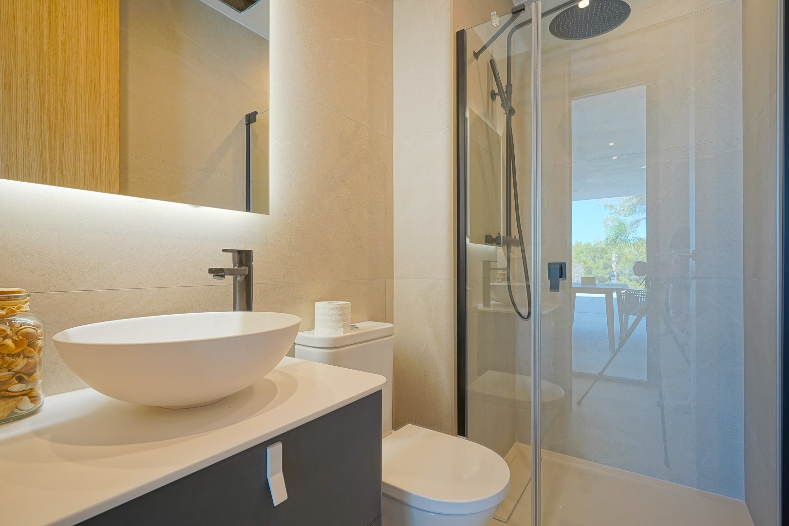 Salle de bain moderne avec vasque à poser, miroir rétroéclairé et douche à l'italienne. Les tons beiges et la robinetterie noire soulignent un design épuré et lumineux.