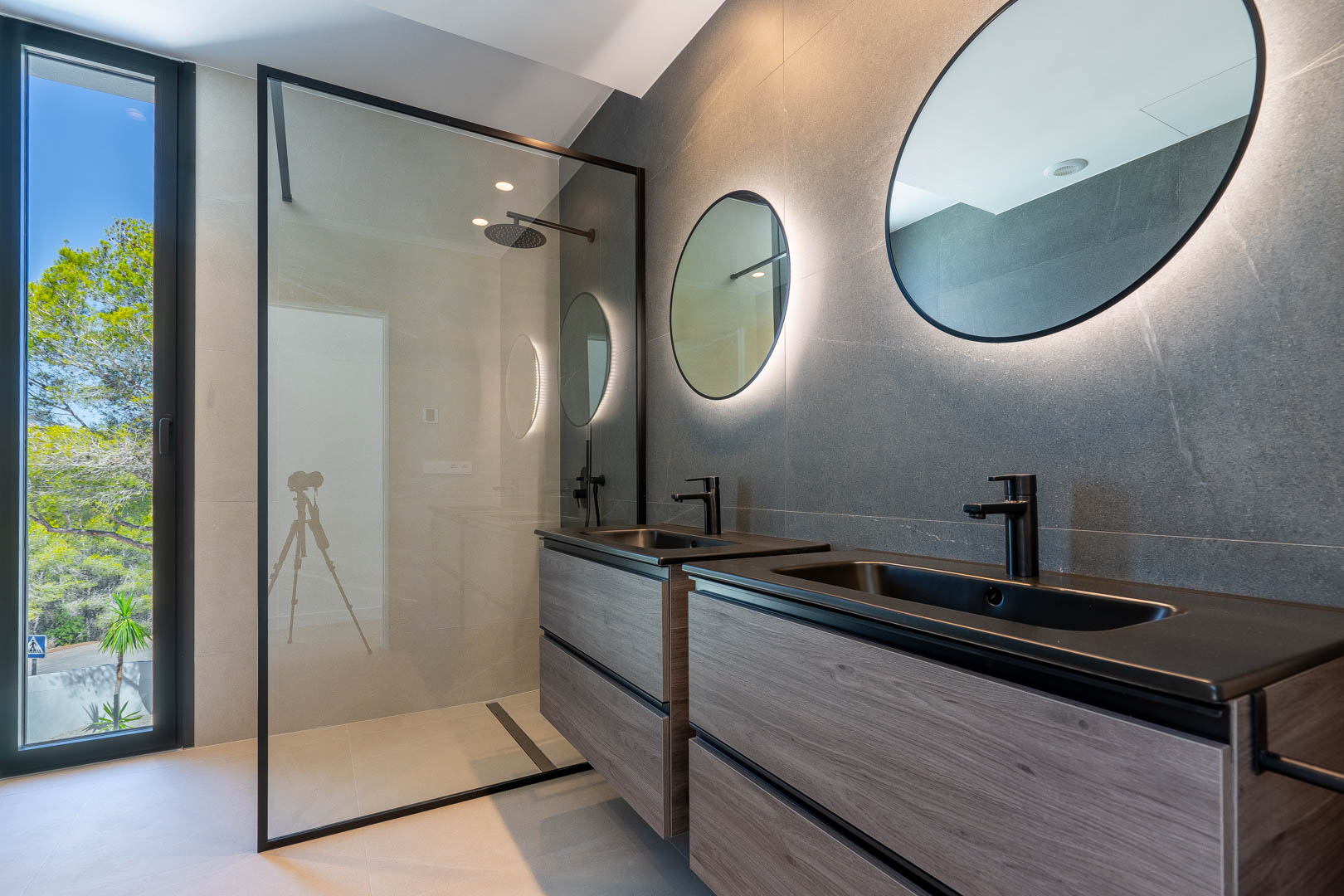 Salle de bain moderne dotée d'un meuble double vasque en bois, de miroirs rétroéclairés et d'une douche à l'italienne avec robinetterie noire.
