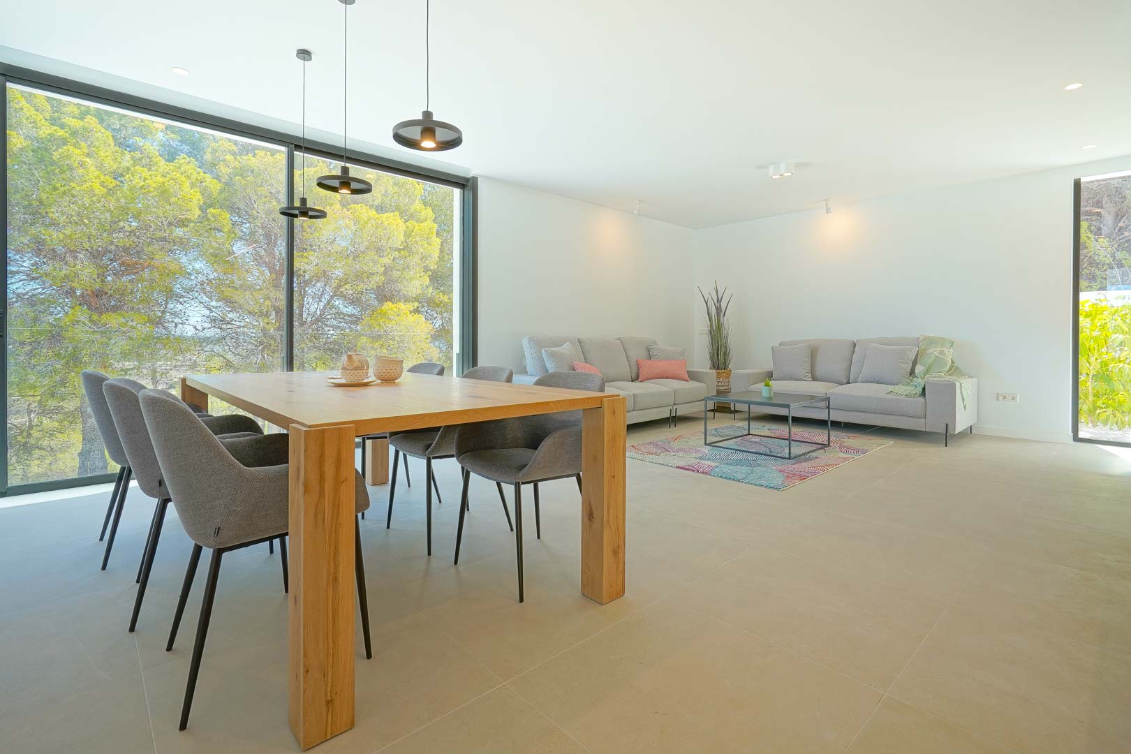 Salon-salle à manger lumineux avec mobilier contemporain et larges baies vitrées offrant une vue apaisante sur la zone boisée environnante.