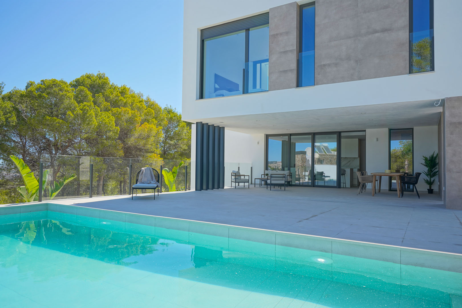 Terrasse principale avec piscine, salon de jardin et coin repas, intégrée dans une architecture moderne aux lignes épurées entourée de pins.