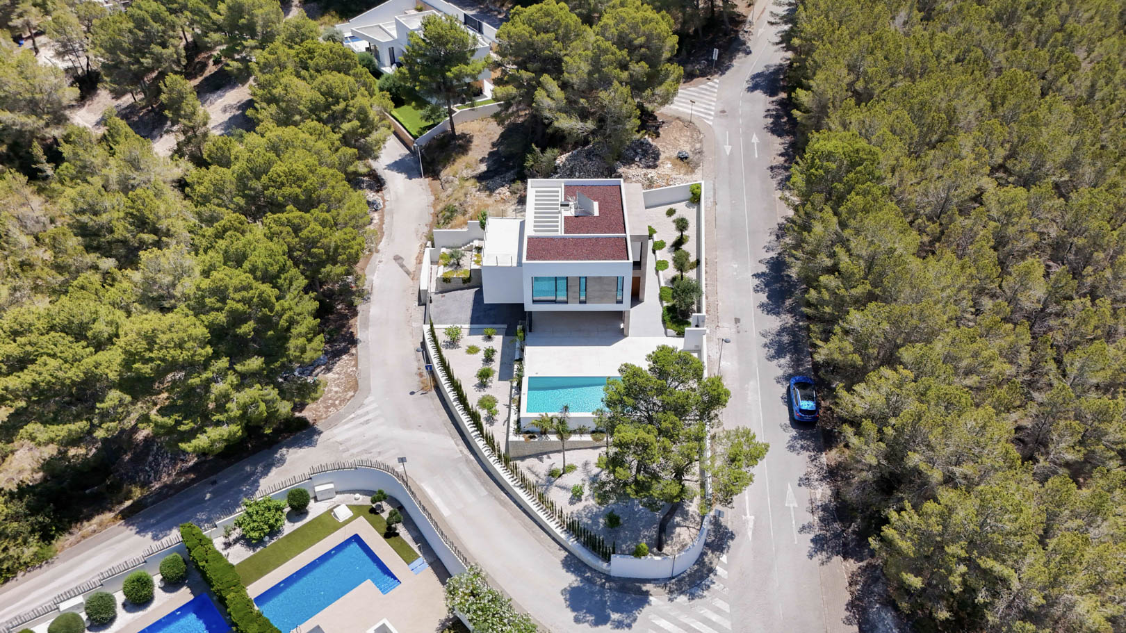 Vue aérienne de la villa moderne nichée dans une pinède, mettant en valeur son architecture blanche, sa piscine rectangulaire et son jardin méditerranéen.