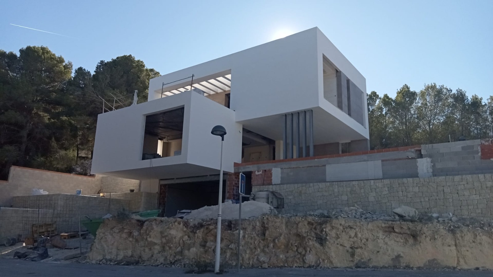 Vue extérieure de la villa en construction, illustrant une architecture cubiste aux volumes en porte-à-faux sur un mur de soutènement en pierre.