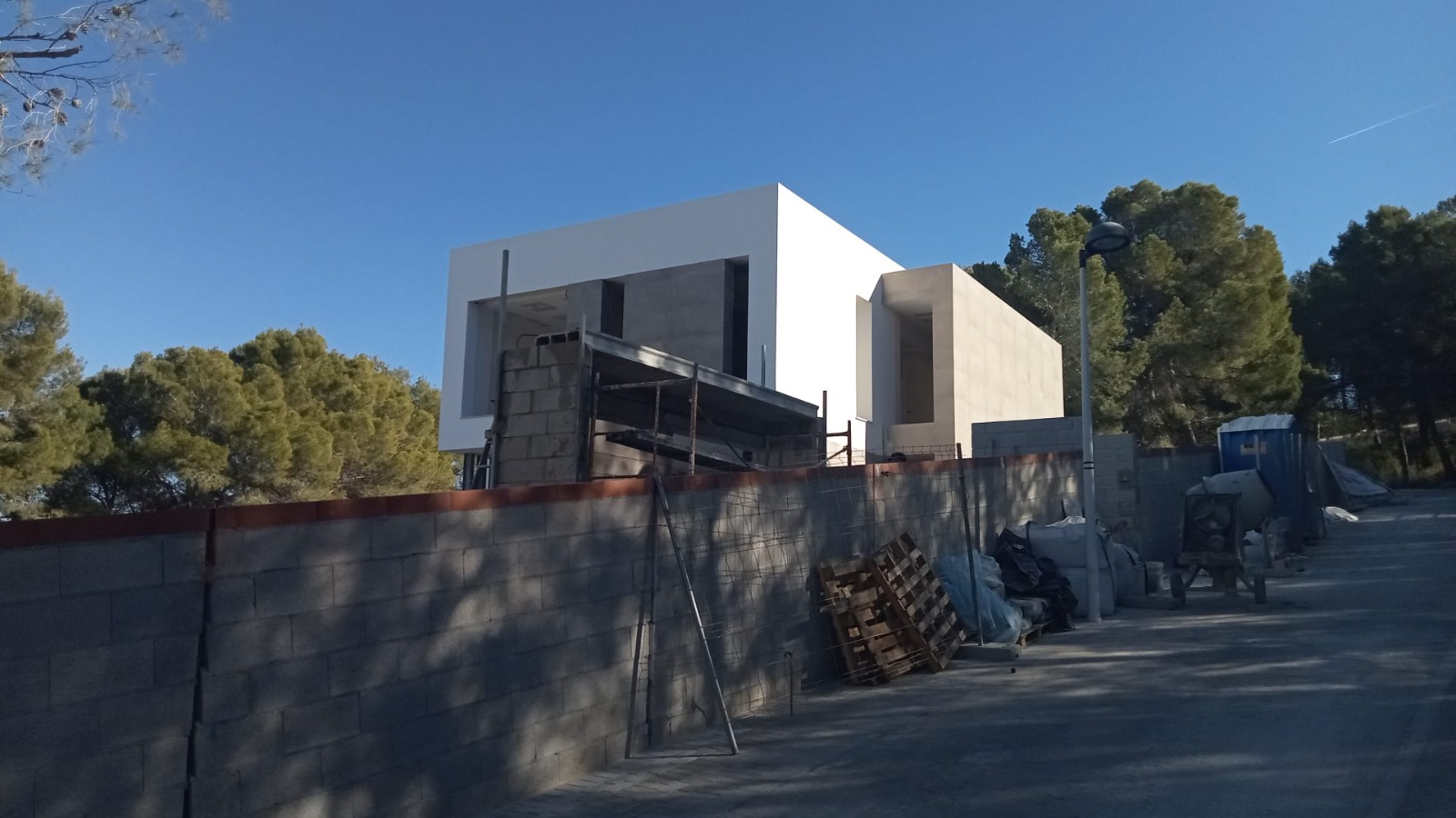 Vue extérieure de la villa moderne en cours de construction, révélant une architecture cubique épurée avec des finitions en pierre naturelle et blanc.