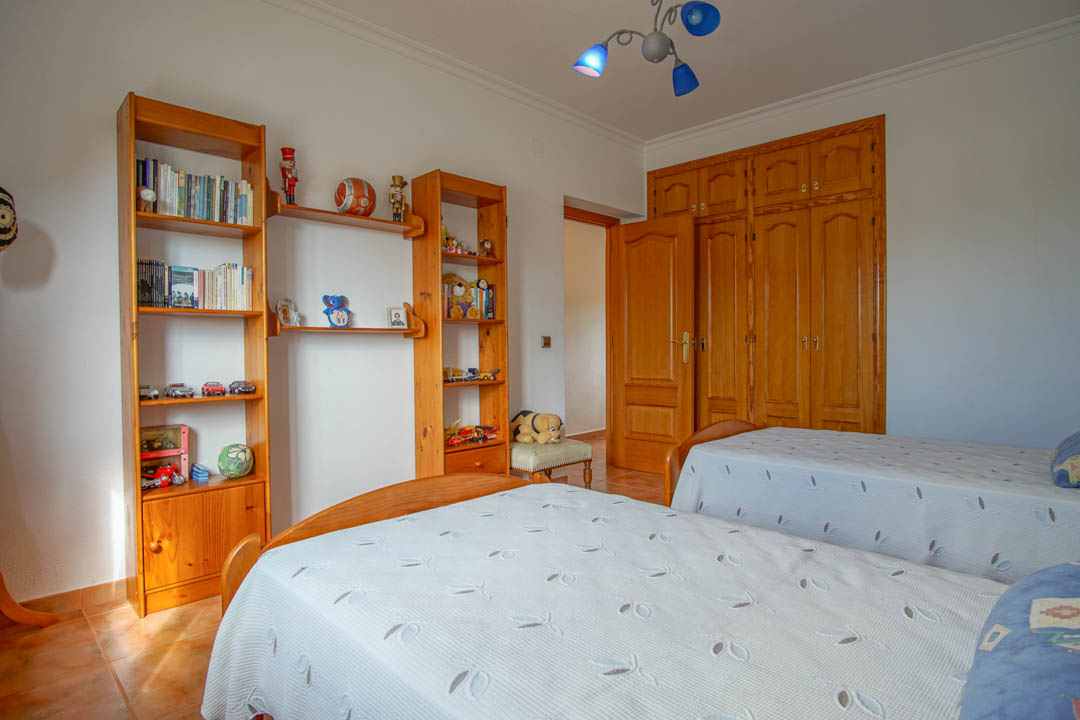 Chambre avec deux lits simples, étagères en bois massif et grands placards encastrés sur mesure aux finitions traditionnelles.