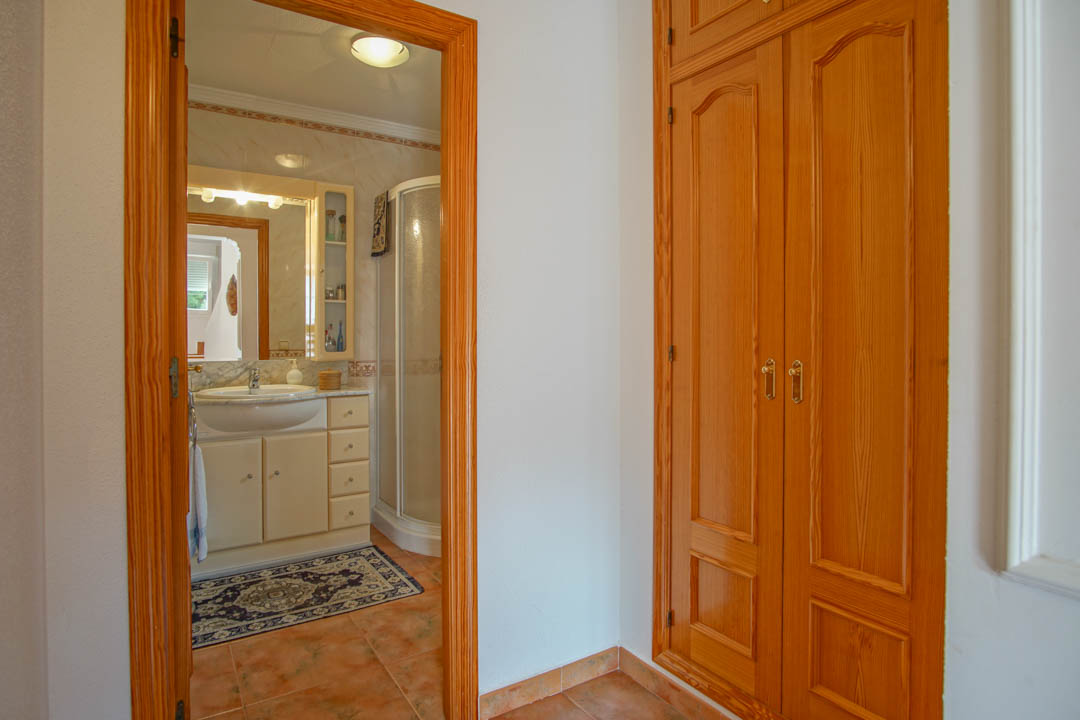 Chambre avec placard intégré en bois massif et salle de bain attenante disposant d'une douche d'angle et d'un plan de toilette en marbre.