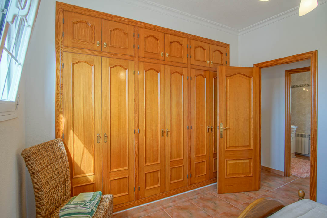 Chambre avec un grand placard intégré en bois massif du sol au plafond et des portes intérieures assorties sur un sol carrelé.
