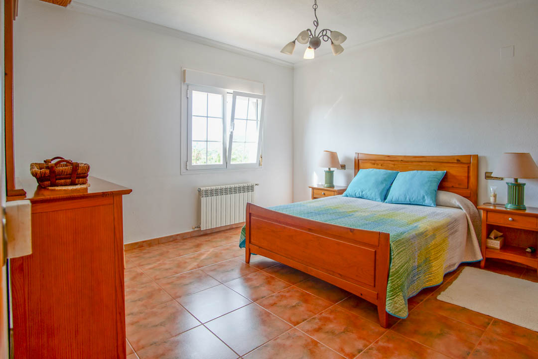 Chambre lumineuse avec mobilier en bois massif, sol en grès cérame rustique et fenêtre à double vitrage équipée d'un radiateur.