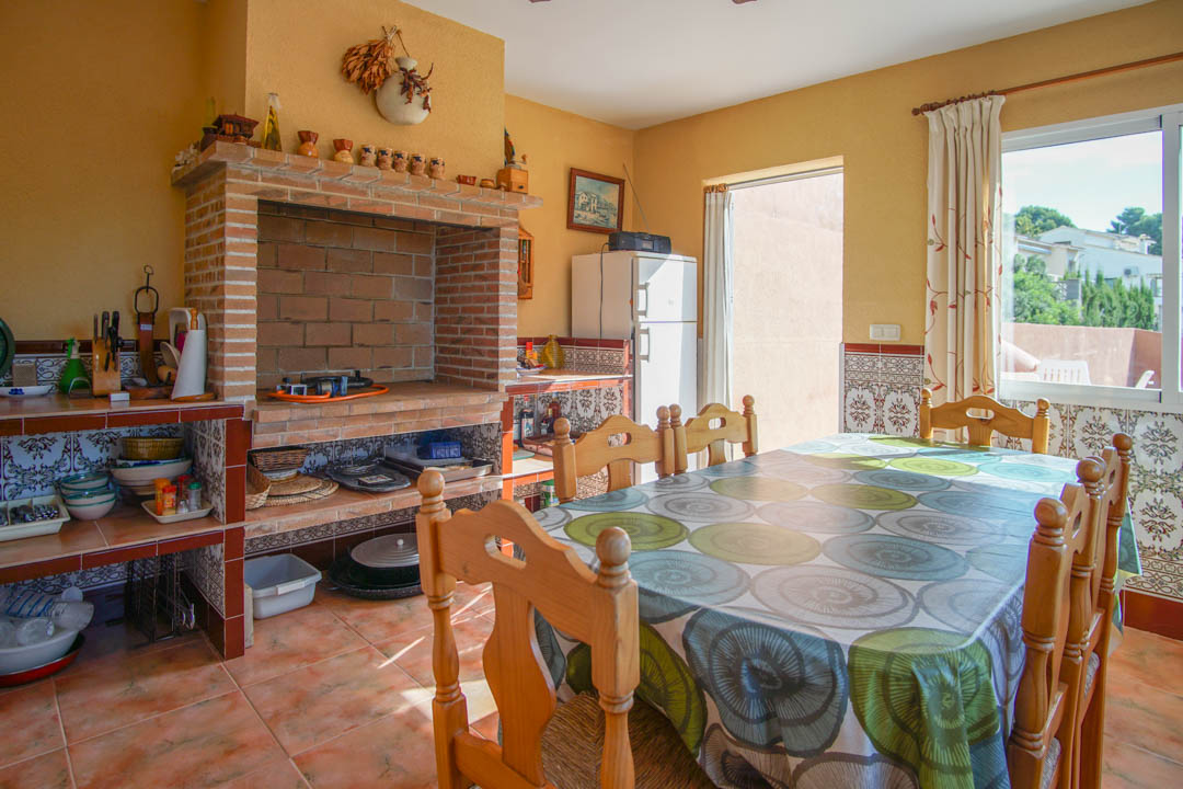 Cuisine d'été fermée avec four à bois en briques, plans de travail carrelés de motifs traditionnels et coin repas avec mobilier en bois massif.