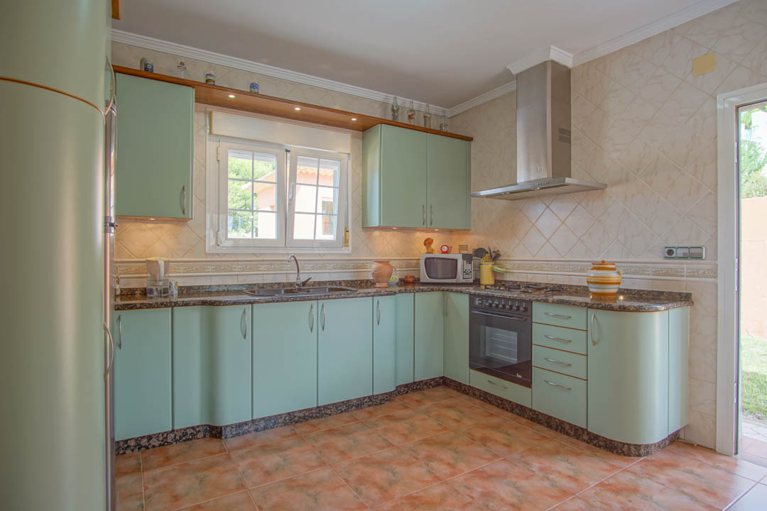 Cuisine indépendante avec des armoires vert menthe aux finitions arrondies, un plan de travail en granit et des murs carrelés avec éclairage sous les meubles.