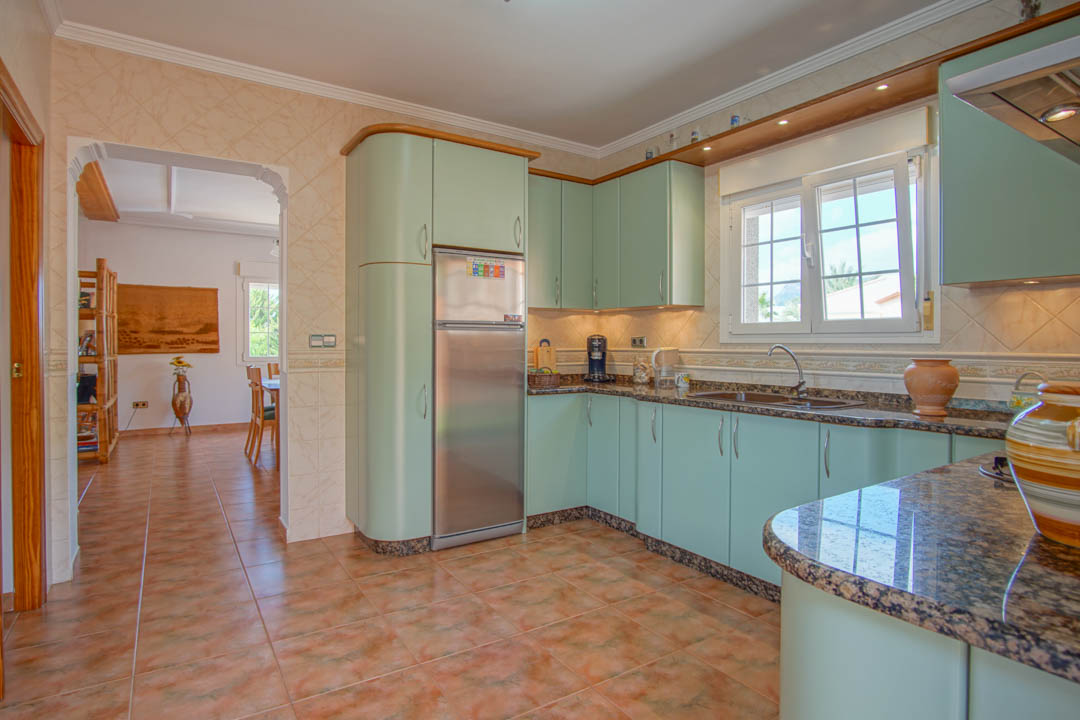 Cuisine indépendante avec des meubles vert menthe, des plans de travail en granit et un sol en céramique. Une arche s'ouvre sur la salle à manger, offrant un espace fonctionnel.