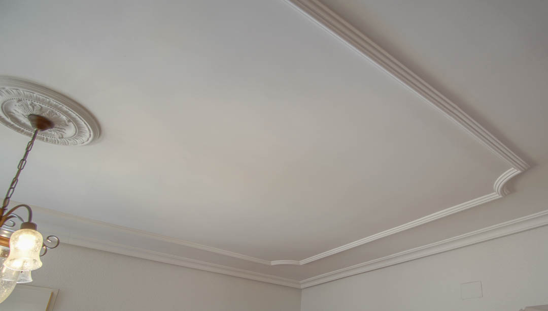 Détail du plafond avec des moulures décoratives en plâtre, un panneau en retrait aux angles arrondis et une rosace classique pour le luminaire.