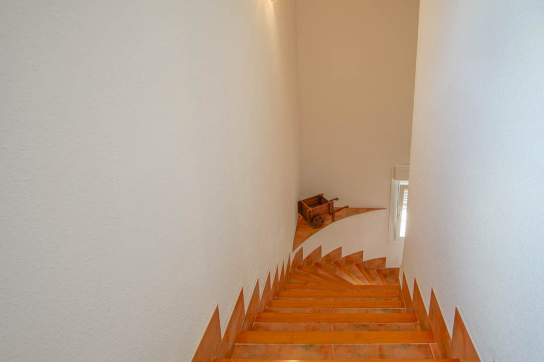 Escalier intérieur avec marches en grès cérame et plinthes assorties, murs blancs texturés et un élément décoratif en bois sur le palier.