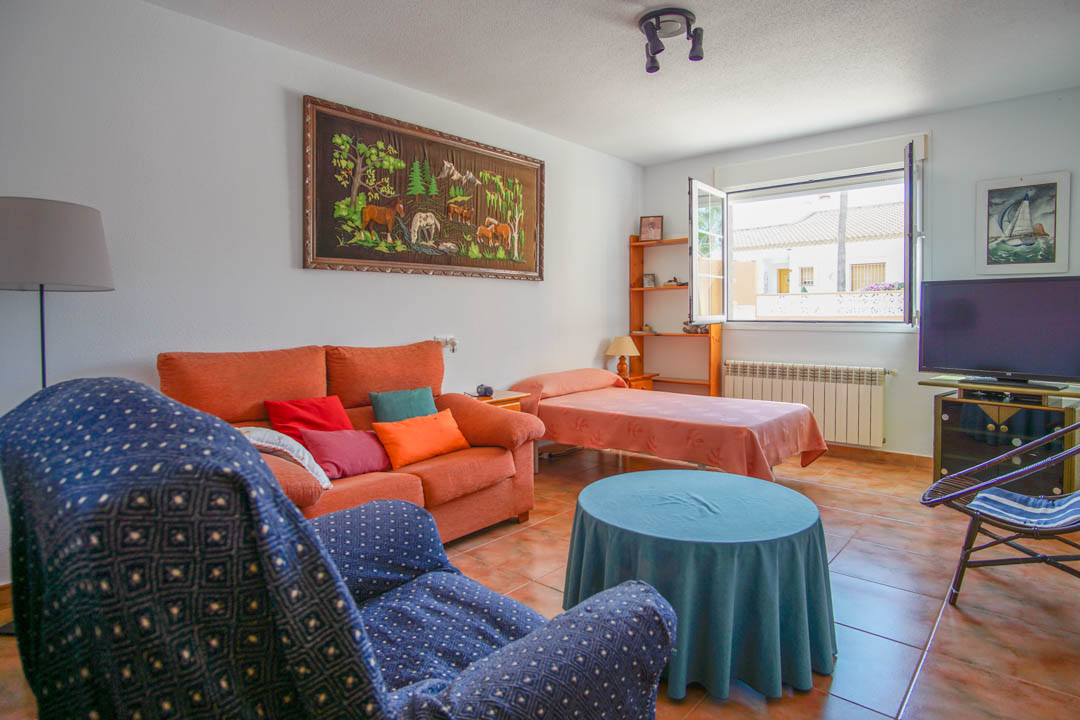 Espace de vie fonctionnel avec sol en céramique, comprenant un coin salon, un lit simple et une grande fenêtre apportant une luminosité naturelle.