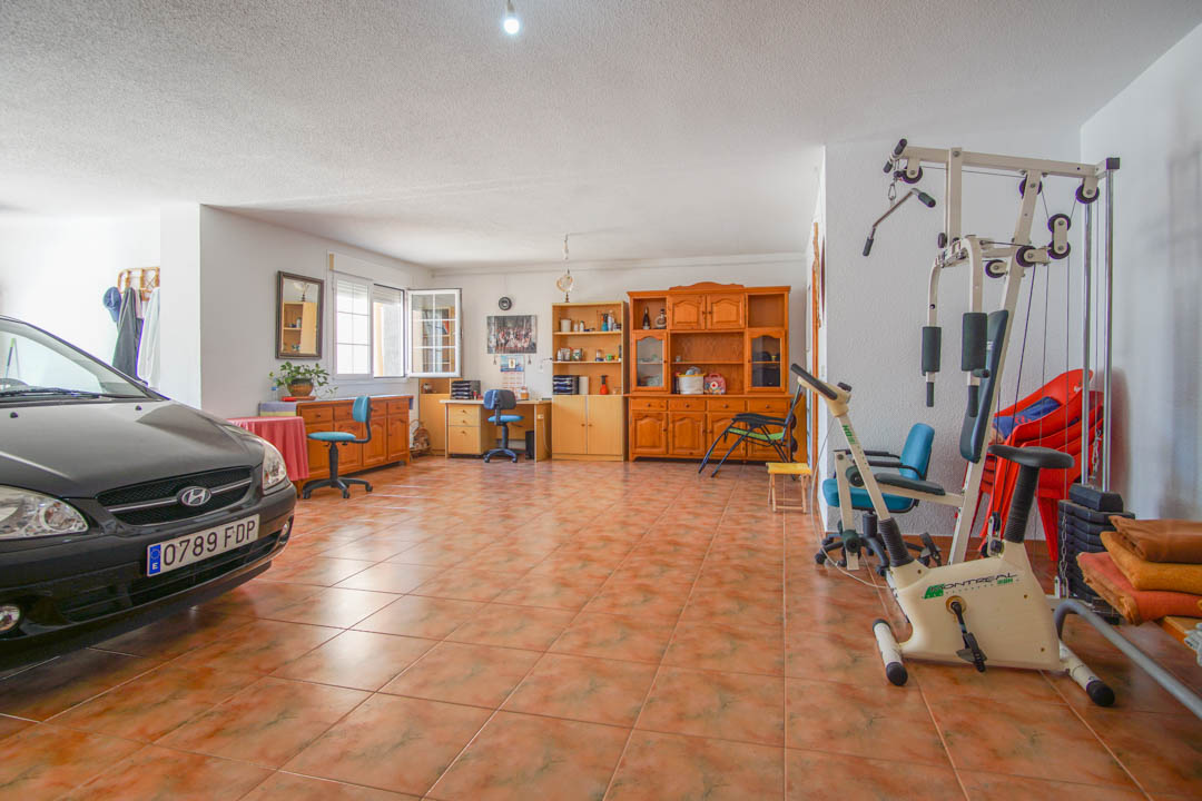 Espace multifonctionnel au rez-de-chaussée avec sol en grès, comprenant un garage, un coin fitness et des meubles de rangement en bois massif de haute qualité.