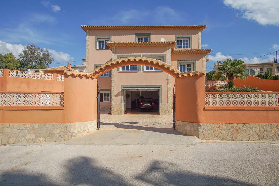 Façade de villa sur trois niveaux avec entrée voûtée, murs d'enceinte couleur terre cuite et garage intégré au rez-de-chaussée.
